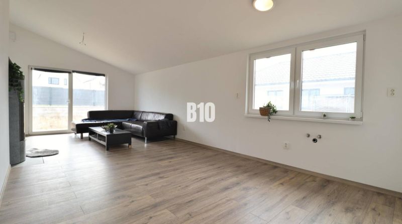 Wohnzimmer in einem Einfamilienhaus, helle Couch, Boden mit Holzdekor, große Fenster.