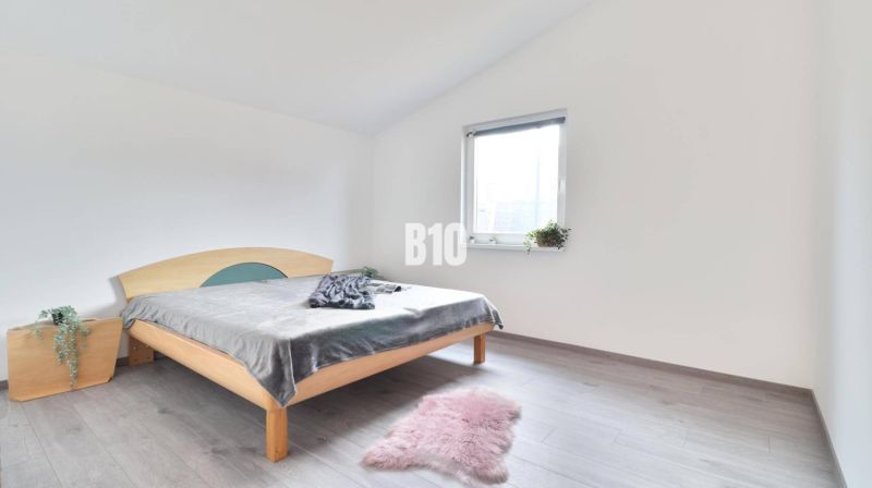 Helles Schlafzimmer im Einfamilienhaus mit Bett, Teppich und Boden in Holzoptik.