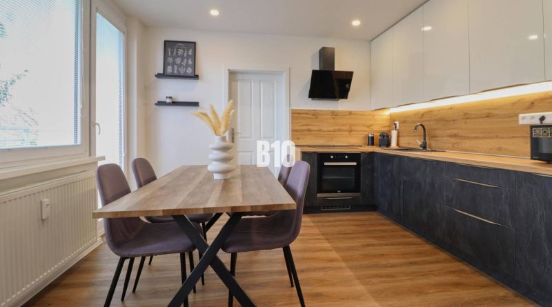 Küche in einer 3-Zimmer-Wohnung mit Holzdekor, Tisch und bunten Stühlen.