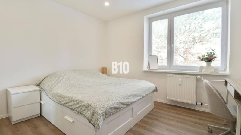 Schlafzimmer in einer 3-Zimmer-Wohnung mit Bett, Schreibtisch und Boden in Holzoptik.