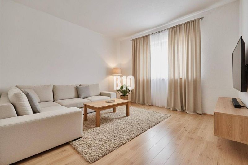 Wohnzimmer eines Einfamilienhauses mit beigem Sofa, Couchtisch und Boden in Holzoptik.