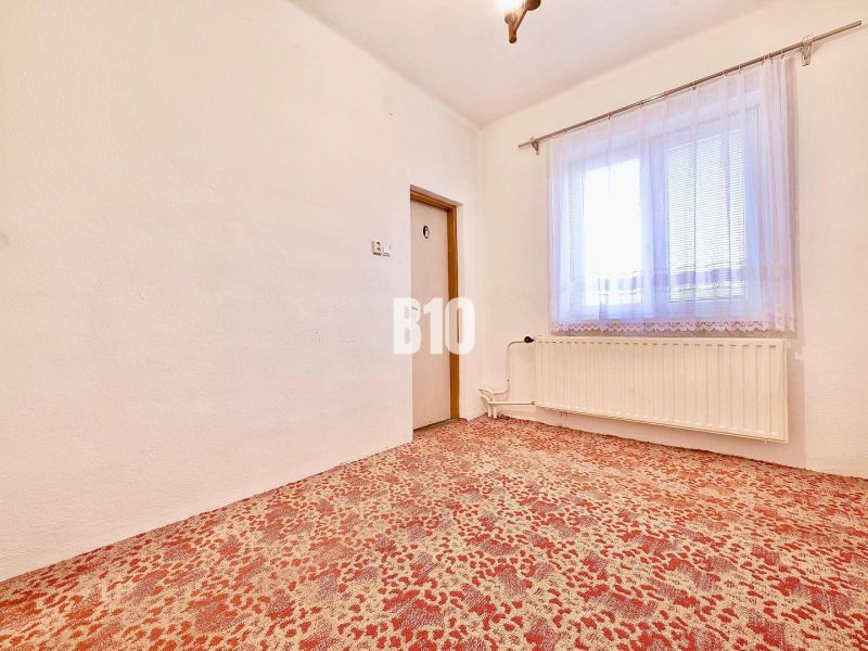 Ein Zimmer in einem Einfamilienhaus mit Teppichboden, Heizkörper und Vorhang am Fenster.