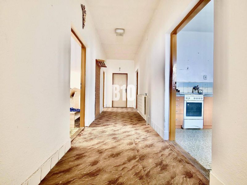Flur im Einfamilienhaus mit Teppich, rechts die Küche, Möbel und Geräte.