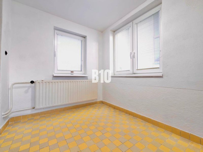 Weiße Wand, Fenster, Heizkörper und gelber Fliesenboden in einem Einfamilienhaus.
