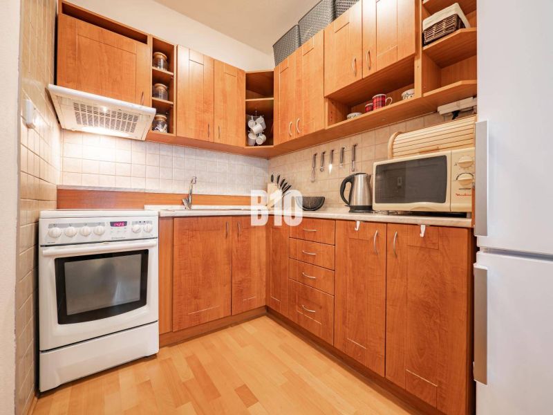 Eine Küche mit Holzschränken, weißen Geräten und einem Boden in Holzoptik in einer 2-Zimmer-Wohnung.