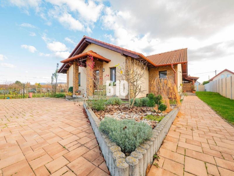 Ein Einfamilienhaus in Nitra mit einem gepflasterten Hof und einem gut gepflegten Garten unter blauem Himmel.