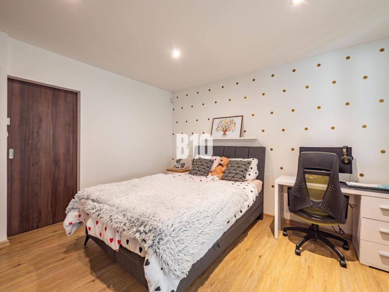 Schlafzimmer in einem Einfamilienhaus mit gepunkteter Tapete, Bett, Tisch und Boden mit Holzdekor.