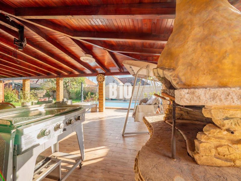 Auf der Außenseite eines Einfamilienhauses in Nitra befindet sich eine überdachte Terrasse mit einem Gartengrill und einem Boden in Holzoptik.