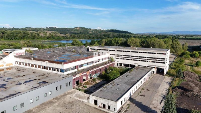Produktionsräume in Levice mit verlassenen Gebäuden, umgeben von Natur und einer Wasserfläche.
