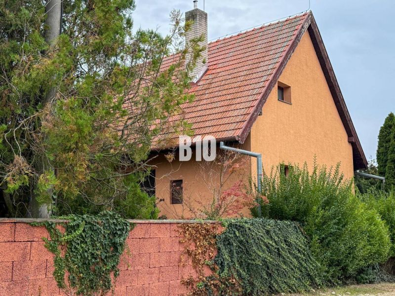 Ein Einfamilienhaus in Vlkas mit rotem Dach, umgeben von Grün und einer Ziegelmauer.
