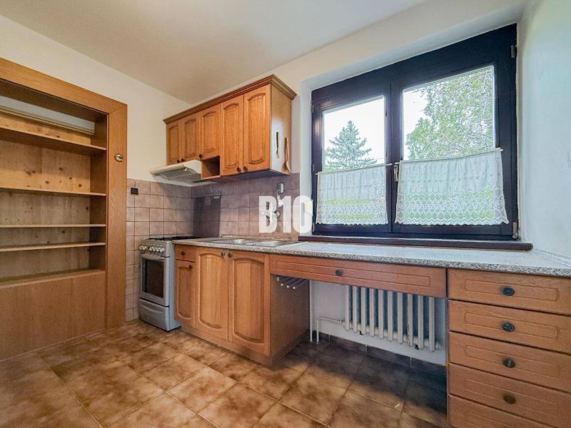Küche in einem Einfamilienhaus mit Holzschränken und großem Fenster, Boden mit Holzdekor.