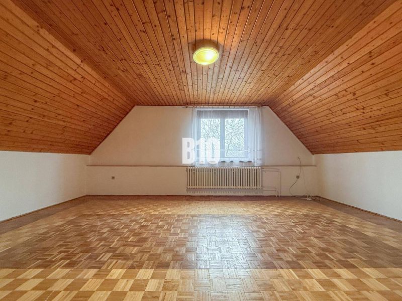 Ein Dachzimmer in einem Einfamilienhaus mit einer Holzdecke und einem Boden mit Holzdekor.