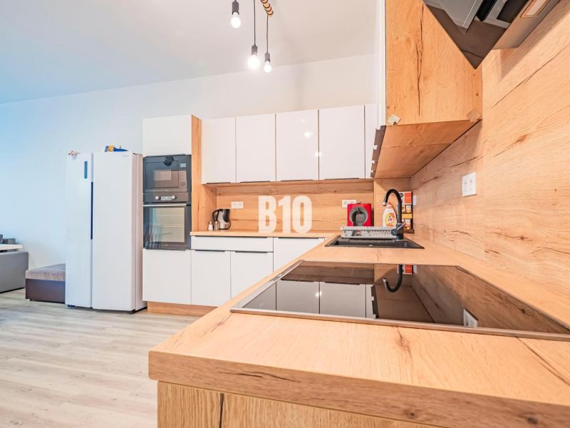 Küche in einer 3-Zimmer-Wohnung mit glänzenden weißen Schränken und einem Boden in Holzoptik.