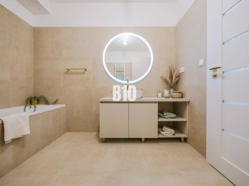 Badezimmer mit rundem Spiegel und beigen Fliesen in einer 2-Zimmer-Wohnung.