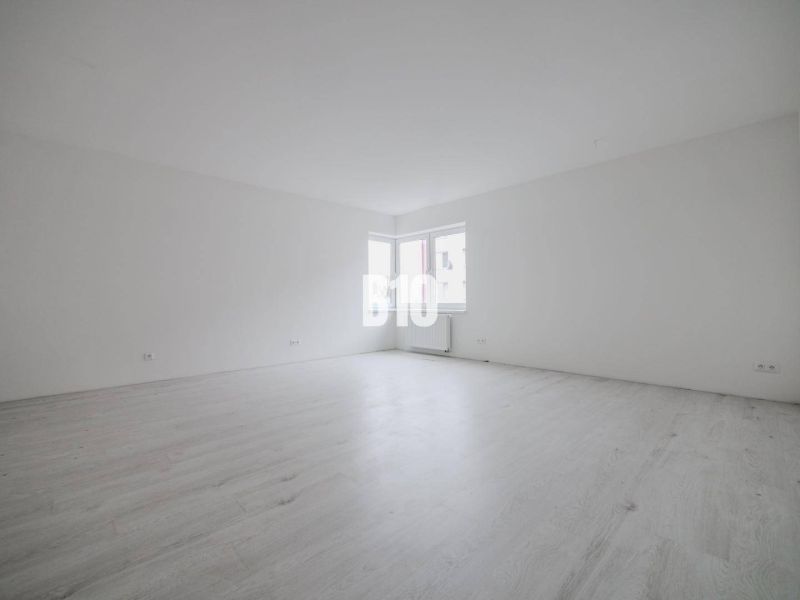 Ein geräumiges Zimmer mit weißen Wänden und einem großen Fenster in einer Einzimmerwohnung.