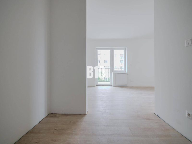 Helles leeres Interieur mit Holzboden und großem Fenster in einem Einzimmerapartment.