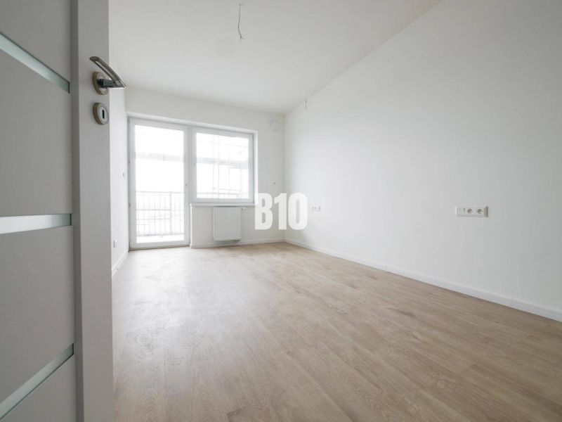 Ein geräumiges Zimmer mit einem großen Fenster, hellem Boden und weißen Wänden in einer 2-Zimmer-Wohnung.
