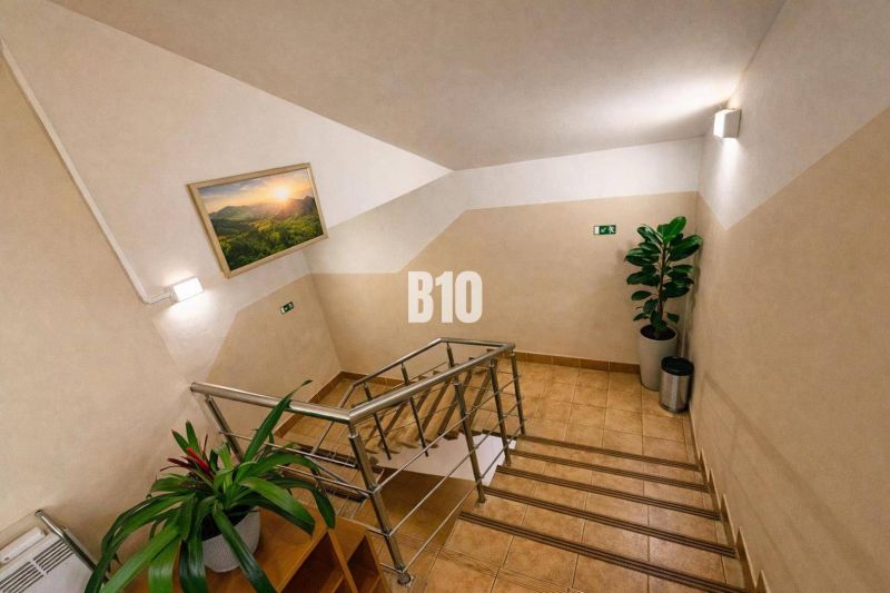 Innenraum eines Gebäudes mit Blumen, Treppe und einem Naturbild an der Wand.