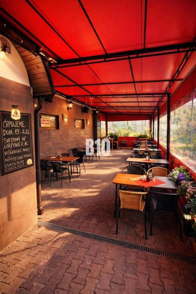 Überdachte Terrasse des Restaurants im Gebäude der Stadt Čadca mit Ziegelpflaster, Blumen und Tischen.