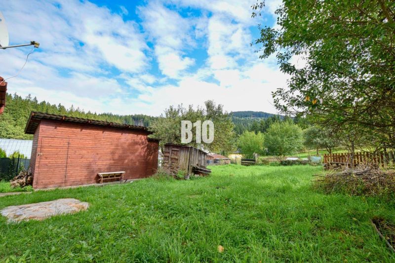 Der Garten eines Einfamilienhauses in Makov mit Holzunterständen und grünen Bäumen in der Umgebung.