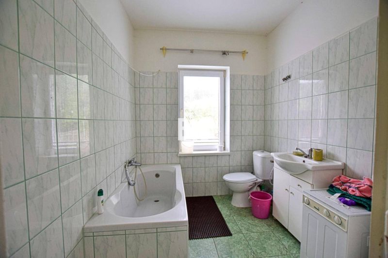Ein Badezimmer in einem Einfamilienhaus mit einer Badewanne, einem Waschbecken und einer Waschmaschine, gefliest mit hellen Fliesen.