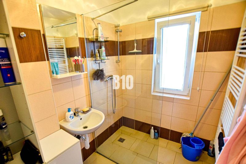Ein Badezimmer in einer Hütte mit Waschbecken, Duschkabine, hohem Fenster und Stauraum.