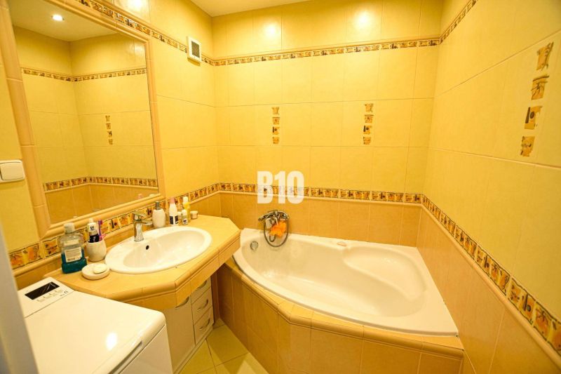 Badezimmer mit gelben Fliesen, Badewanne, Waschbecken und Spiegel in einer 3-Zimmer-Wohnung.