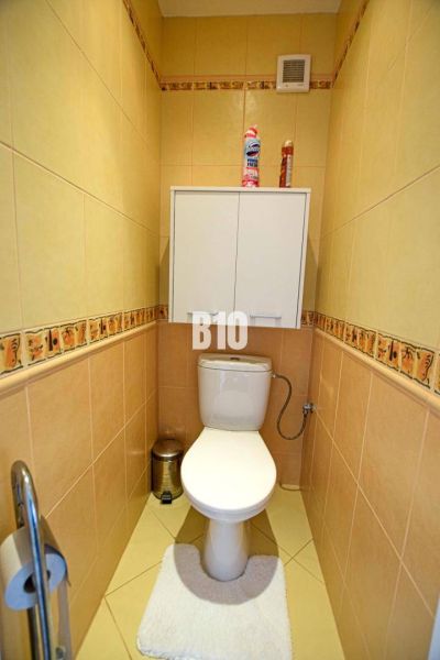 Toilette mit beigen Fliesen und einem Wandschrank in einer 3-Zimmer-Wohnung.