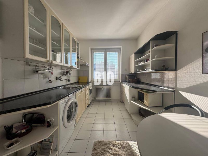 Küche in einer 2-Zimmer-Wohnung mit weißen Schränken und schwarzer Arbeitsplatte.
