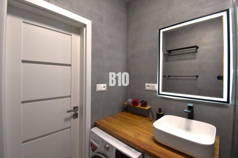 Badezimmer mit Waschbecken, Spiegel und Boden mit Holzdekor in einer 3-Zimmer-Wohnung.