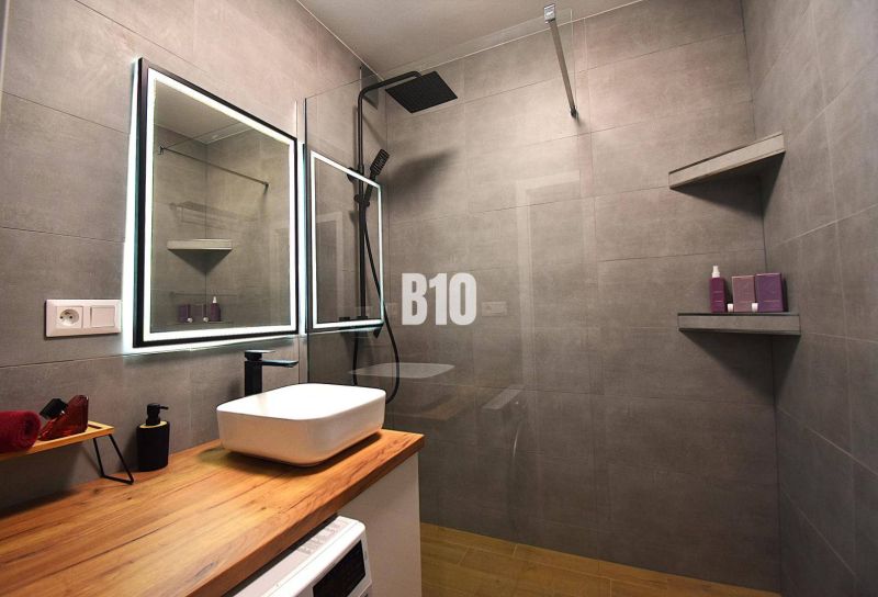 Ein Badezimmer in einer 3-Zimmer-Wohnung mit einer großen Dusche und einem Boden in Holzoptik.