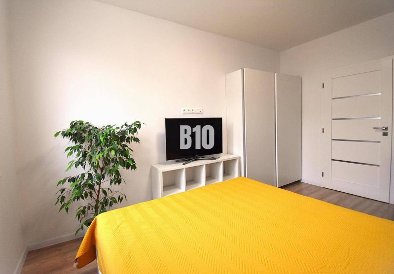 Schlafzimmer in einer 3-Zimmer-Wohnung mit Fernseher, Schrank und Boden in Holzoptik.