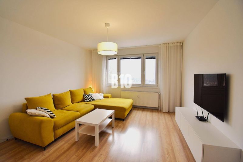 Wohnzimmer in einer 3-Zimmer-Wohnung mit einem markanten gelben Sofa und einem Boden in Holzoptik.