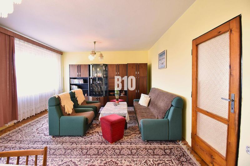 Wohnzimmer in einem Einfamilienhaus mit Sofas, Sesseln, Vitrine und Teppich.