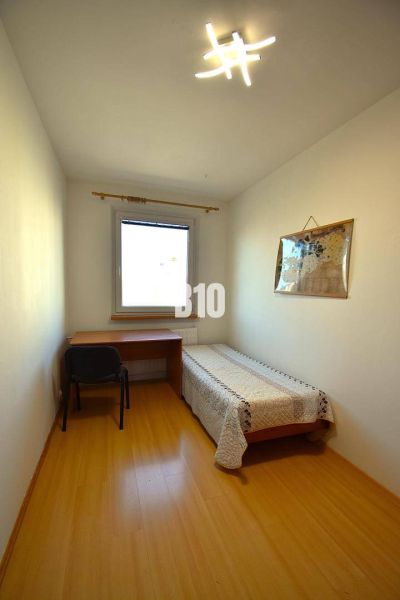 Einfaches Zimmer mit Tisch, Bett und Boden in Holzoptik in einer Wohnung mit mehr als 5 Zimmern.