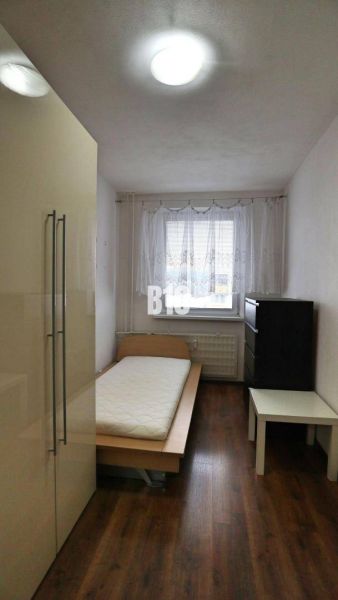 Einfach eingerichtetes Zimmer mit einem Einzelbett und Holzboden in einer 4-Zimmer-Wohnung.