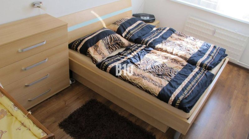 Schlafzimmer mit gemusterten Bettbezügen, Kommode und Boden mit Holzdekor in einer 4-Zimmer-Wohnung.