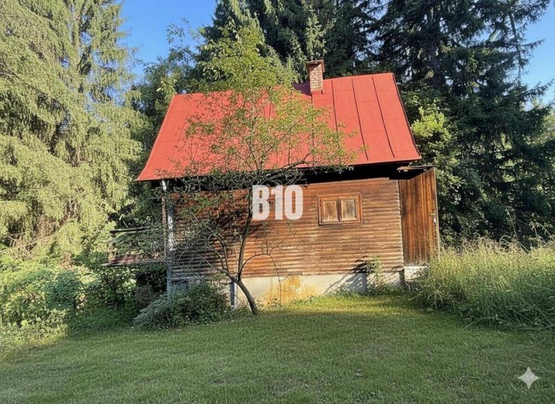 Eine Holzhütte in Kunerad mit rotem Dach, umgeben von Wäldern und Wiesen.