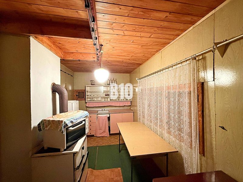 Eine Küche in einer Hütte mit Holzdecke und antikem Herd, ergänzt durch einen Vorhang.