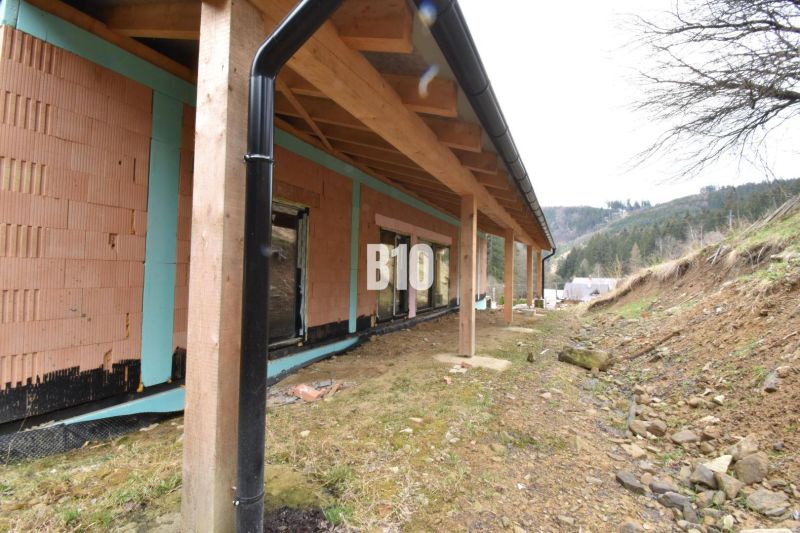 Ein im Bau befindliches Einfamilienhaus mit einem hölzernen Unterstand, ebenem Gelände und umliegender Landschaft.