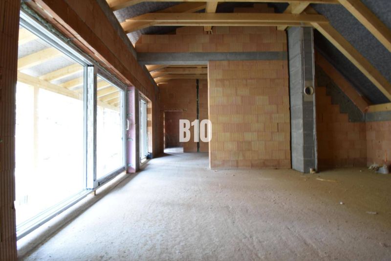 Unvollendetes Interieur eines Einfamilienhauses mit großen Fenstern und Ziegelwänden.