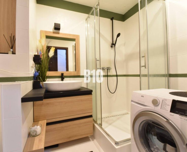 Das Badezimmer in der 3-Zimmer-Wohnung enthält eine Dusche, ein Waschbecken und eine Waschmaschine.