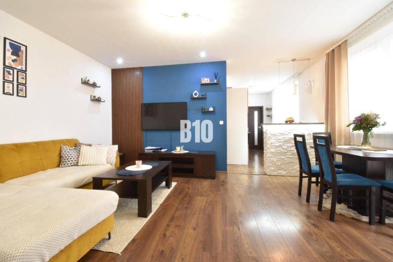 Wohnzimmer mit Sofa und Esstisch in einer 3-Zimmer-Wohnung und einem Boden mit Holzdekor.