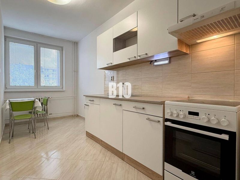 Helle Küche in der Ferienwohnung mit Herd und Tisch mit grünen Stühlen.