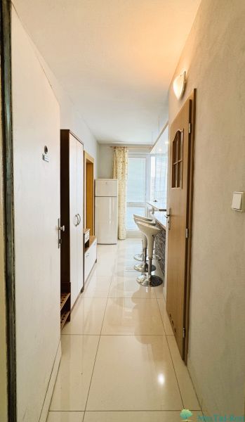 Ein schmaler Flur in einer Einzimmerwohnung mit Barhockern und einem Kühlschrank.