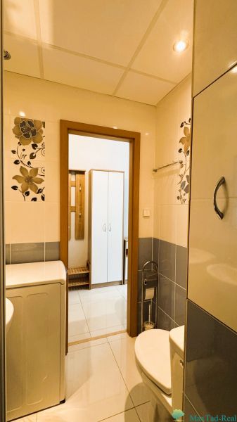 Badezimmer in einer Einzimmerwohnung mit Waschmaschine, Toilette und Blumendekorationen an den Wänden.