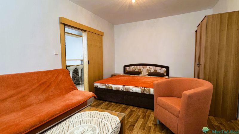 Ein Zimmer mit einem Doppelbett, einem orangefarbenen Sessel und einem Boden in Holzoptik.