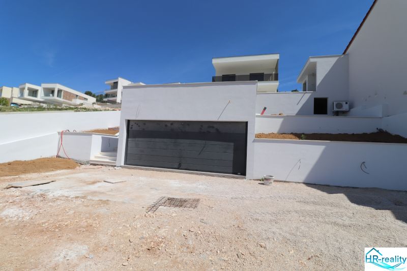 Eine Villa in Žaborić mit weißer Fassade und eingebauter Garage am Hang.