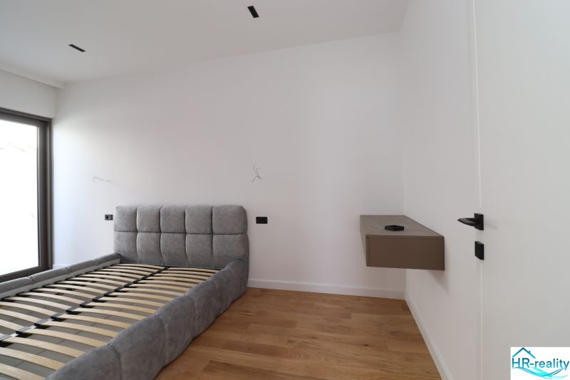 Schlafzimmer in einer Villa mit einem Bett und einem Boden in Holzoptik, schneeweiße Wände.