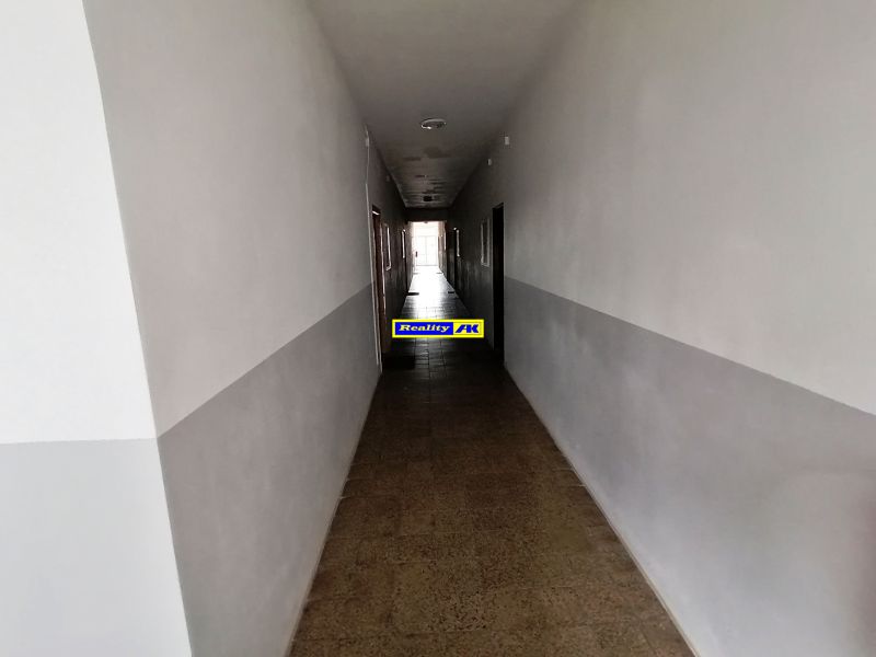 Ein langer Flur mit weißen Wänden und Fliesenboden in einer Einzimmerwohnung.
